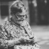 selective focus grayscale photography of woman using phone while sitting at bench